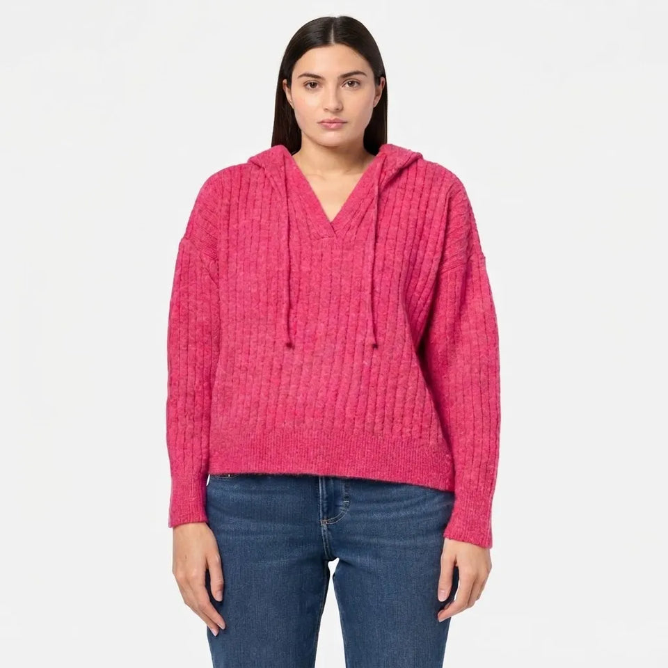 A woman modeling a bright pink ribbed knit pullover hoodie with drawstrings and a V-neck, paired with blue jeans, against a plain white background.