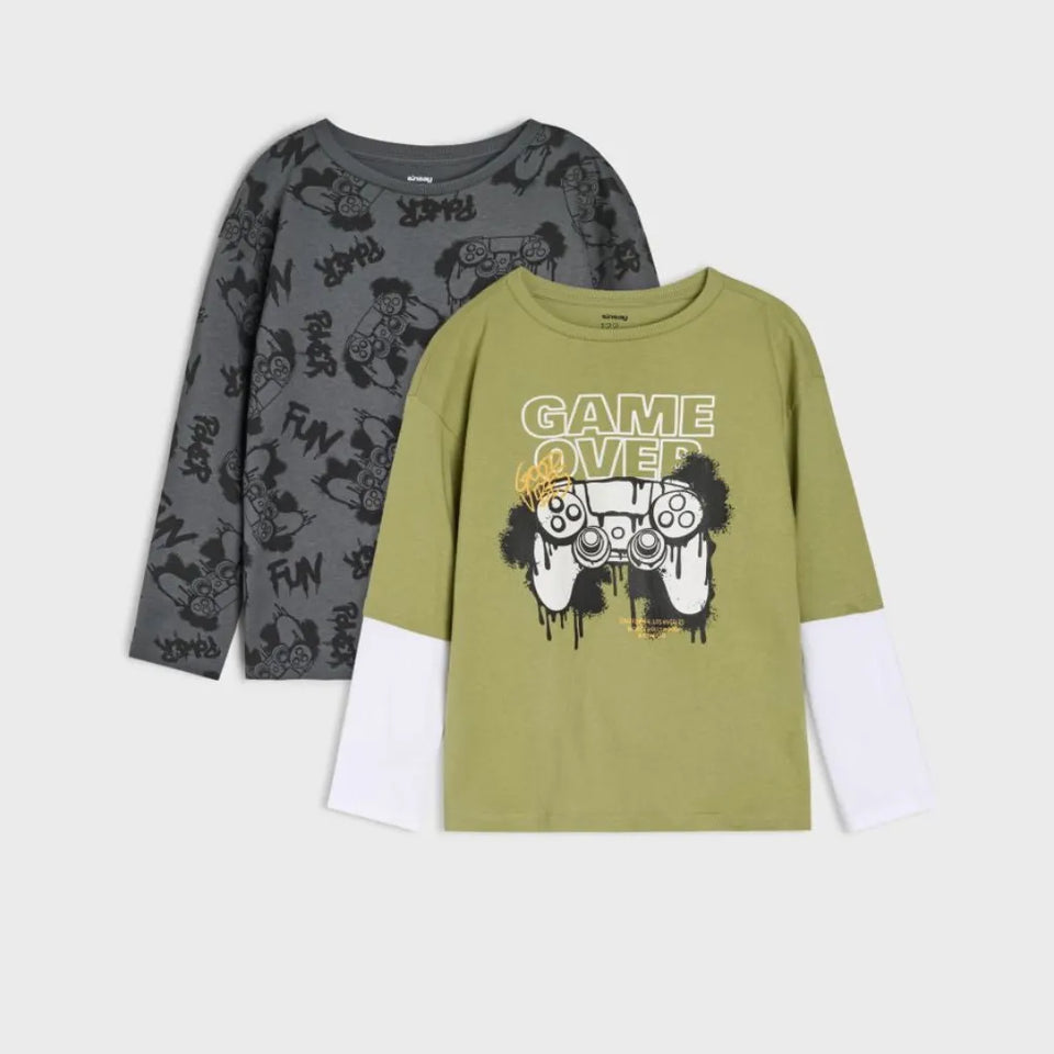 Two long-sleeve graphic shirts displayed on a light gray background. The front shirt is olive green with a white under-sleeve, featuring a 'GAME OVER' graphic with a game controller.