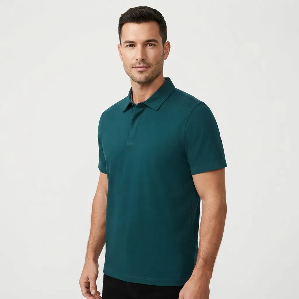 A man wearing a dark teal short-sleeve polo shirt, standing against a light gray studio background.