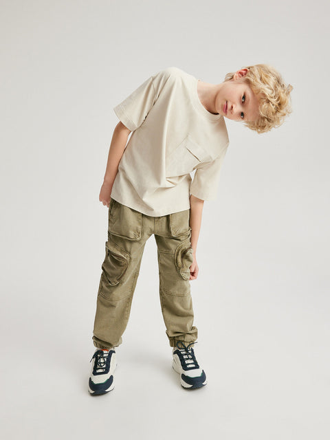 Child wearing a beige t-shirt and cargo pants on a white background