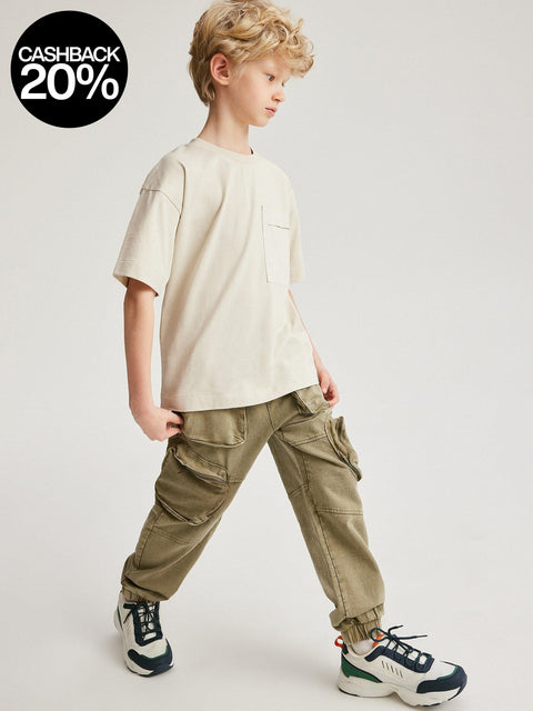 Child wearing a beige t-shirt and green cargo pants on a plain background