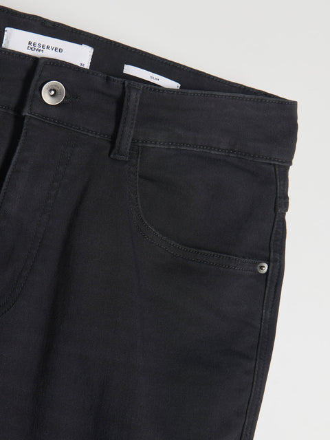 Close-up of black pants with a 'Reserved' label on a light gray background