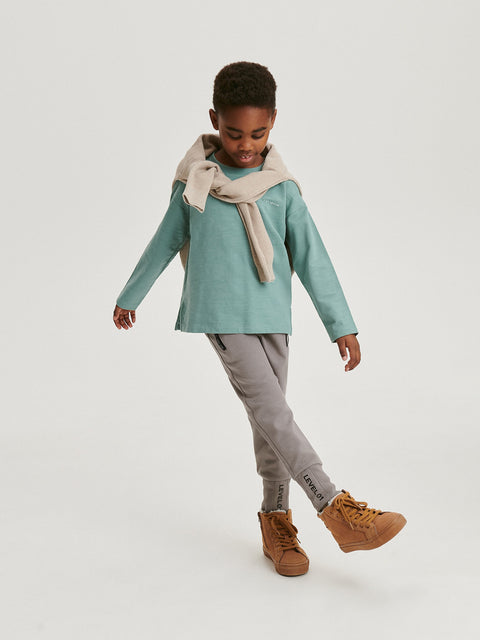Child wearing a teal sweater, gray pants, and brown boots on a white background