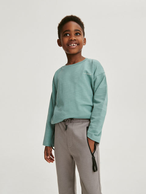 Child wearing a light green sweatshirt and gray pants on a white background