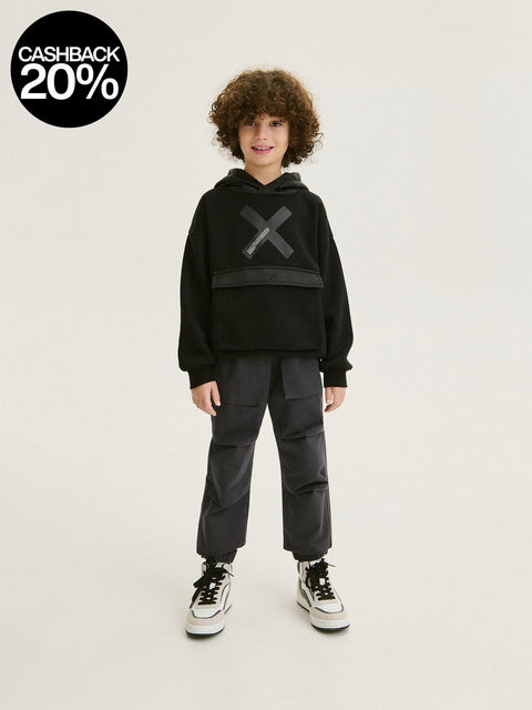 Child wearing a black hoodie with a logo and dark pants on a white background, with a cashback 20% badge.