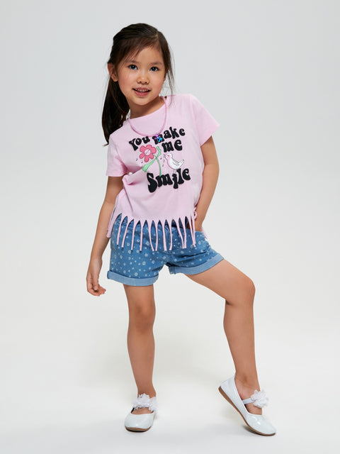 Young girl wearing a pink t-shirt with text and denim shorts on a white background
