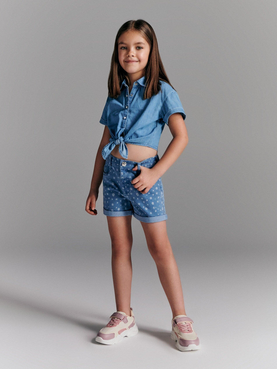 Young girl wearing a blue denim outfit with polka dot shorts on a gray background