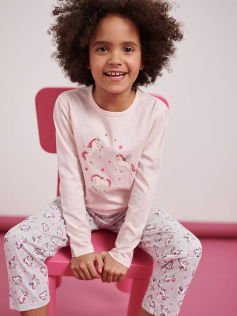 Child wearing pink pajamas with unicorn designs sitting on a pink chair against a white background