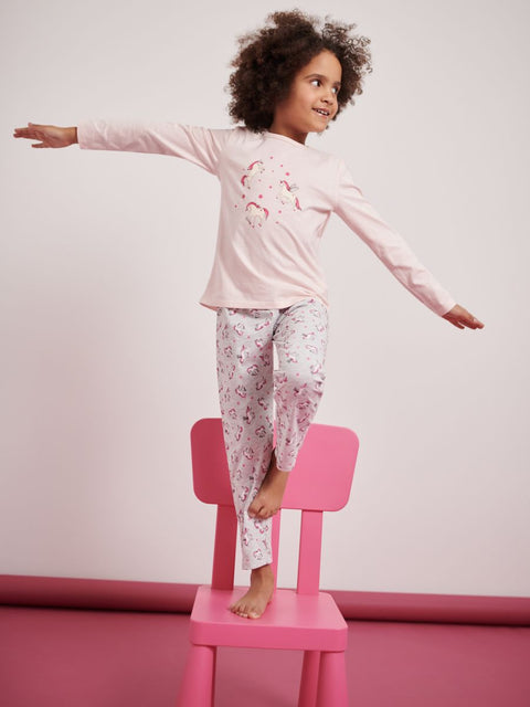 Child wearing pink pajamas with a unicorn design, standing on a pink chair against a light pink background.