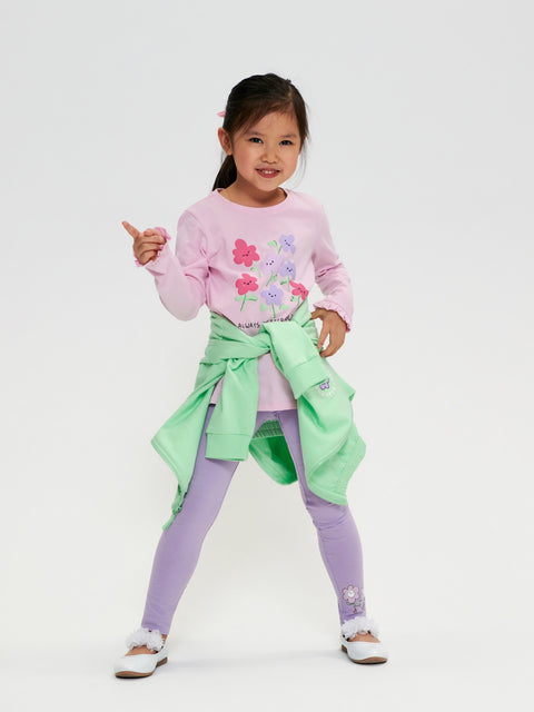 Young girl wearing a pink floral sweater, purple leggings, and green apron on a white background
