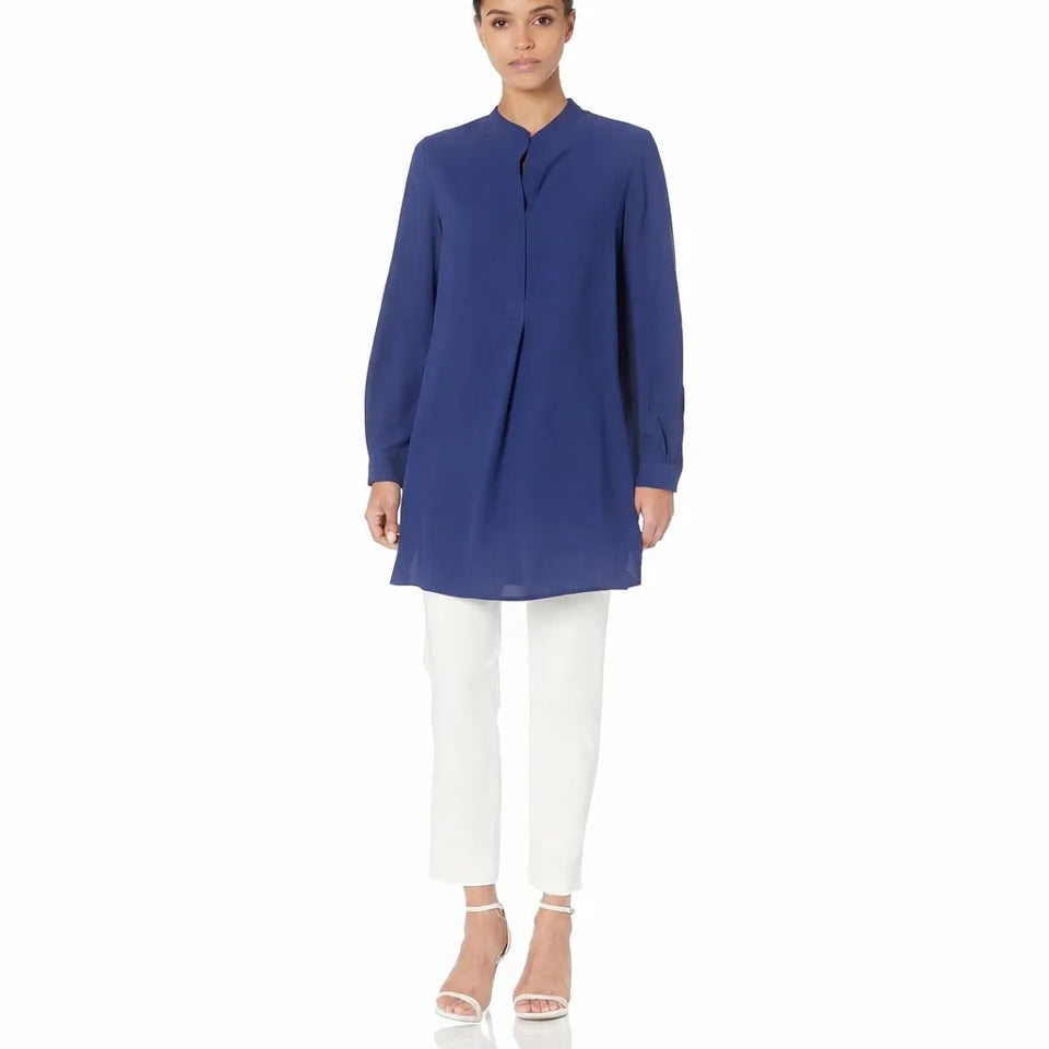 A woman modeling a royal blue long-sleeve tunic top with a mandarin collar, paired with white cropped pants and clear high-heeled sandals, against a plain white background.
