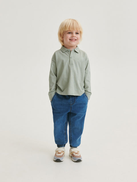 Child wearing a green shirt and blue jeans on a white background