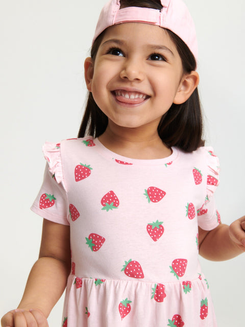 Child wearing a pink dress with strawberry pattern and a matching cap on a light background