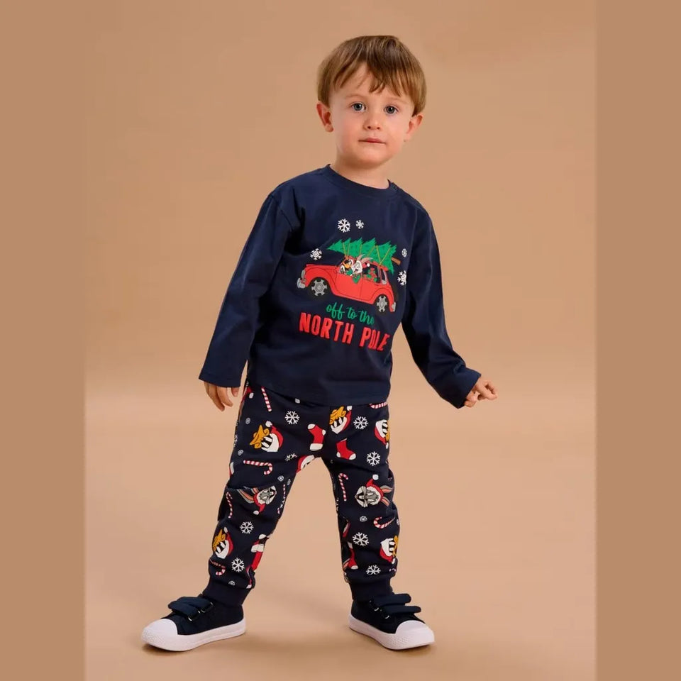 A toddler stands against a plain beige studio background wearing a navy long-sleeve Christmas-themed sweatshirt and matching patterned pants. The sweatshirt has a red truck carrying a green Christmas tree with the words 'We are NORTH PINE' in red.