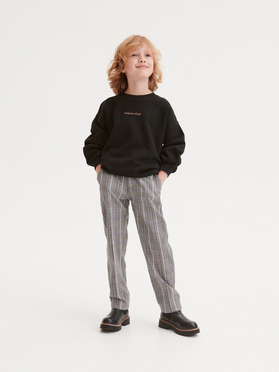 Child wearing a black sweatshirt and plaid pants on a white background