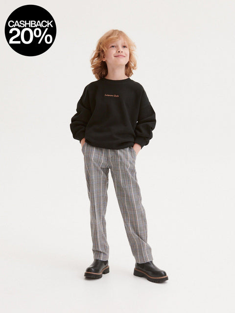 Child wearing a black sweatshirt and plaid pants on a white background