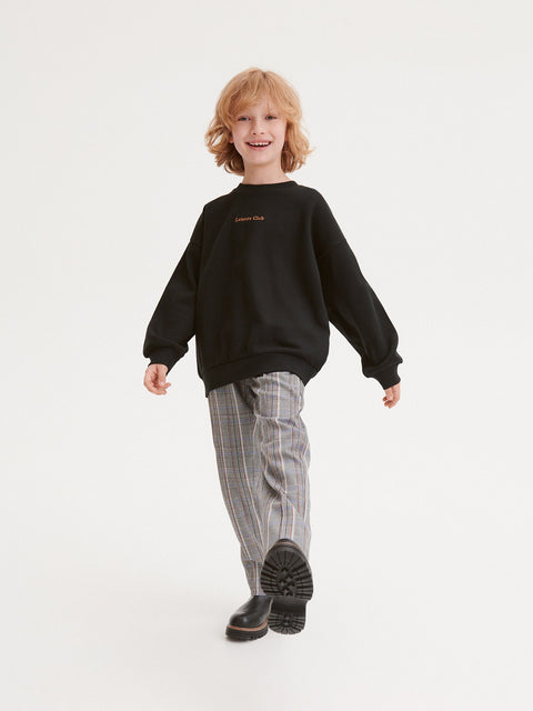 Child wearing a black sweatshirt and checkered pants on a white background