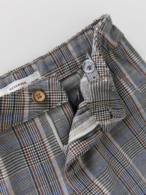 Close-up of a plaid fabric with a button and label on a light gray background