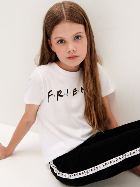 Young girl wearing a white t-shirt with 'FRIENDS' text and black pants with 'FRIENDS' text.