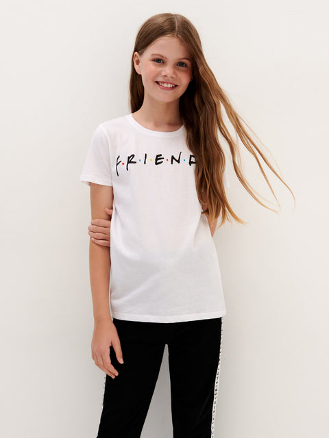Young girl wearing a white t-shirt with 'FRIENDS' printed on it against a plain background