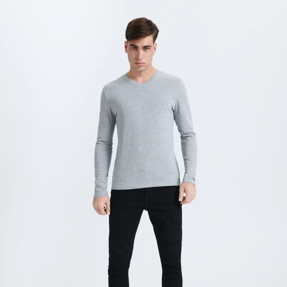 A man modeling a light gray long-sleeve V-neck knit sweater with black pants, standing against a plain white studio background.
