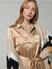 Woman wearing a gold jumpsuit with a patterned cardigan against a gray background
