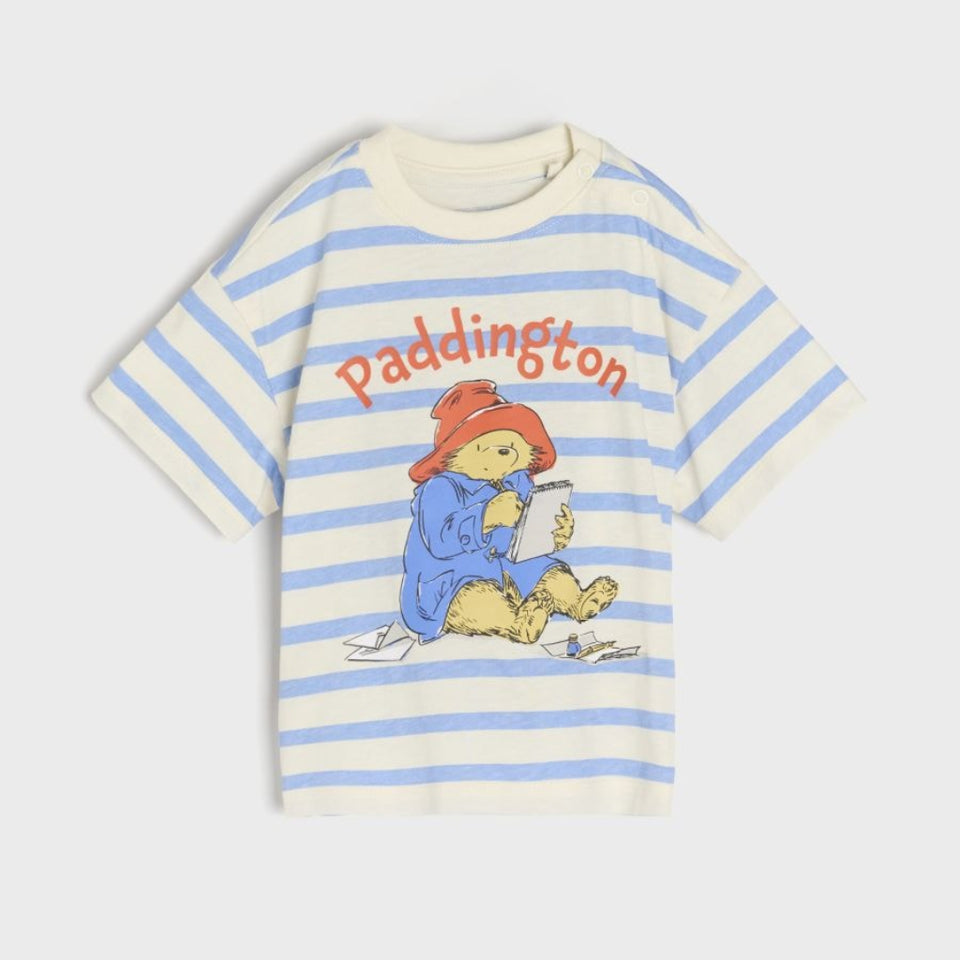 A children's short-sleeve t-shirt with light blue and off-white horizontal stripes, featuring a central graphic of Paddington Bear and the text 'Paddington' in orange.
