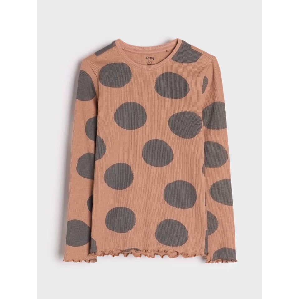 A long-sleeve knit top in a dusty peach-pink color with large dark gray polka dots, featuring a raw, frayed hem and cuffs, shown flat on a light gray background.