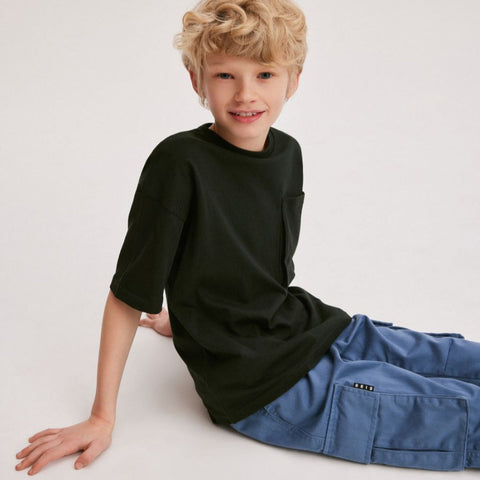 Child wearing a black shirt and blue pants sitting on a white background