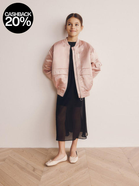 Person wearing a pink jacket over a black dress on a plain background