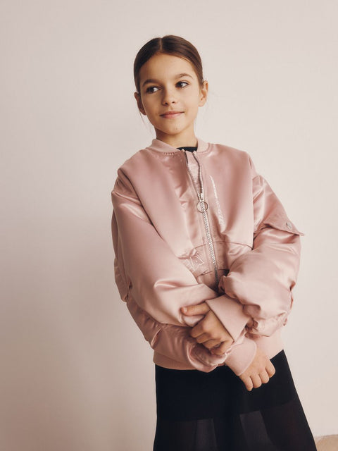 Young girl wearing a pink jacket against a plain background