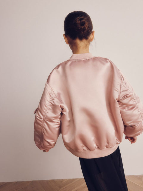 Person wearing a pink satin bomber jacket against a plain background