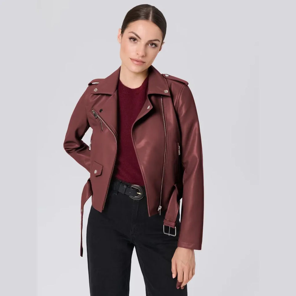 A woman modeling a dark burgundy faux leather moto jacket over a matching burgundy top and black pants, shot against a solid light gray background.