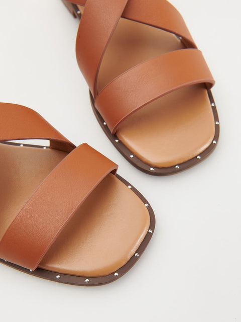 Pair of brown sandals with criss-cross straps on a light gray background