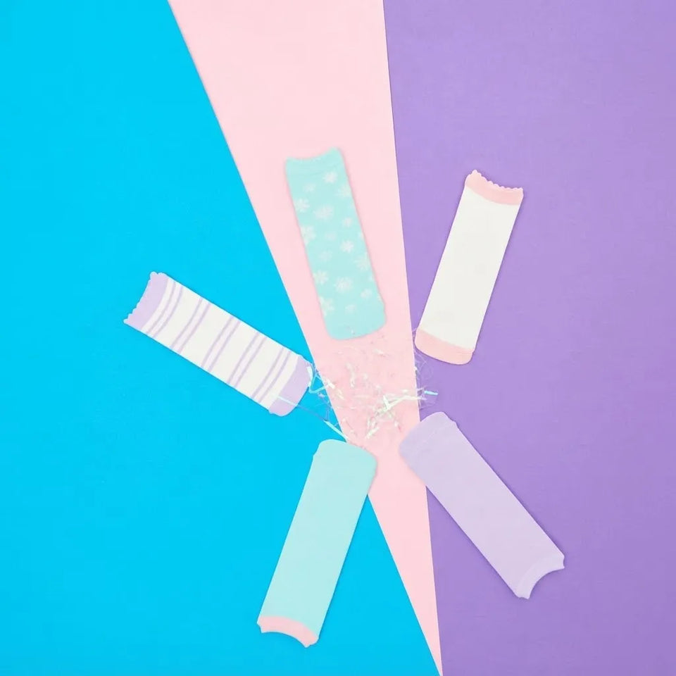 Five reusable menstrual cups in pastel colors, including light blue, lavender, mint, and white, arranged in a radial pattern on a split pink and purple background.