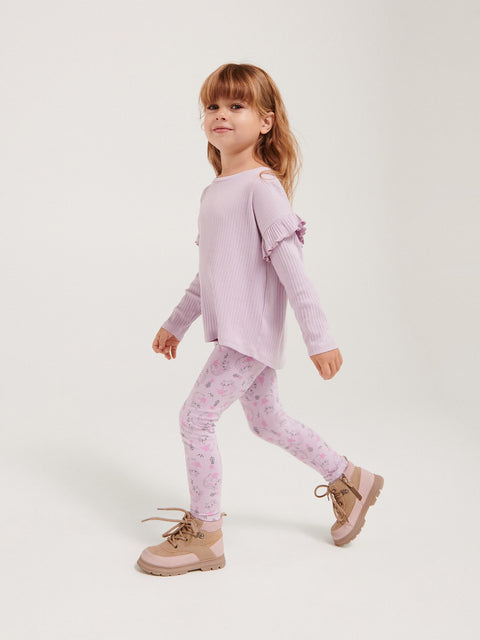 Young girl wearing a light purple outfit with floral leggings on a white background