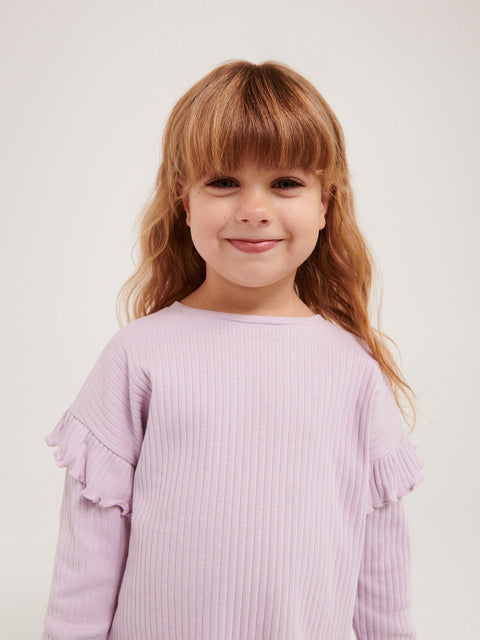 Young girl wearing a light purple ribbed sweater with ruffled sleeves on a plain background