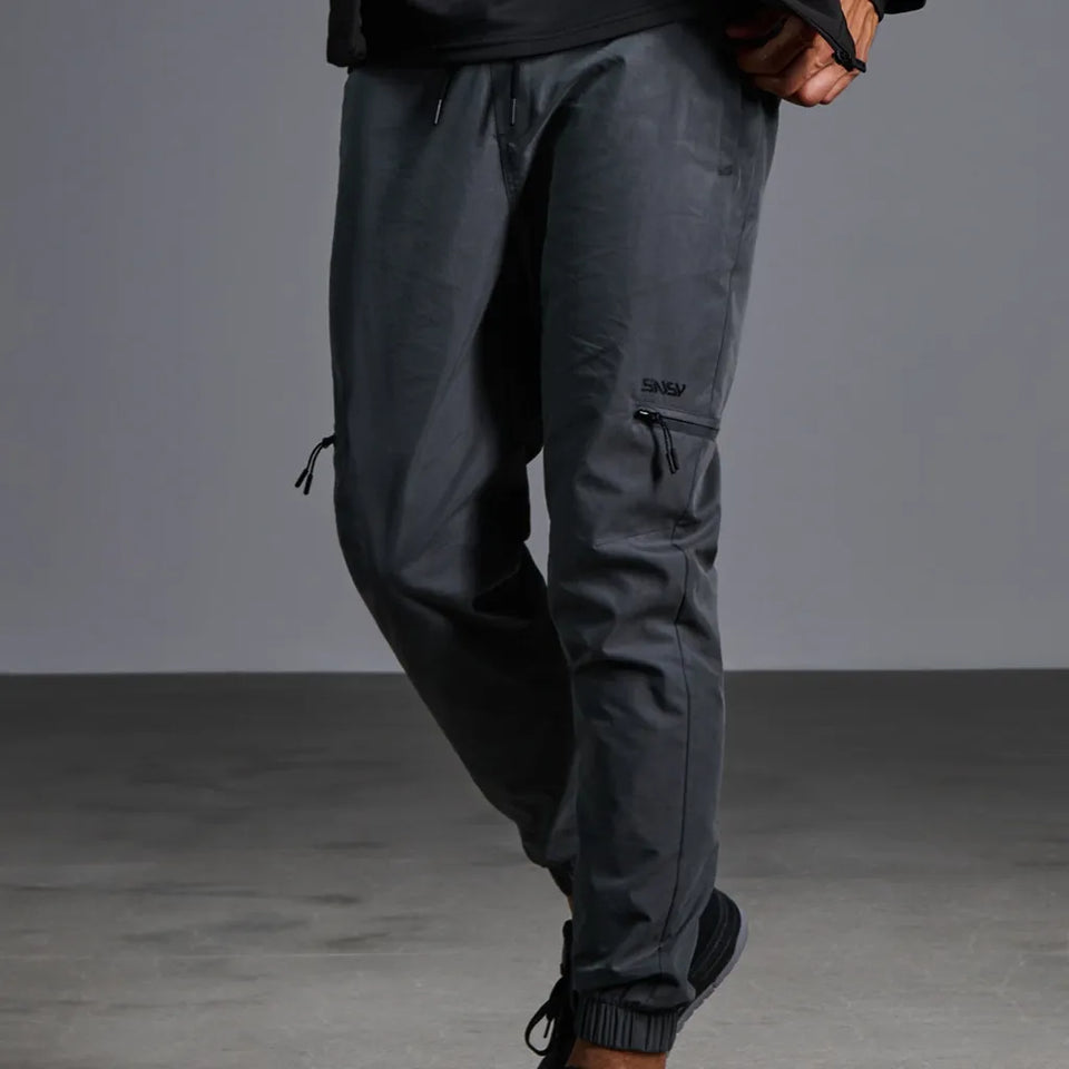Dark gray jogger pants with zippered cargo pockets and elastic cuffs, shown on a model against a gray studio background.