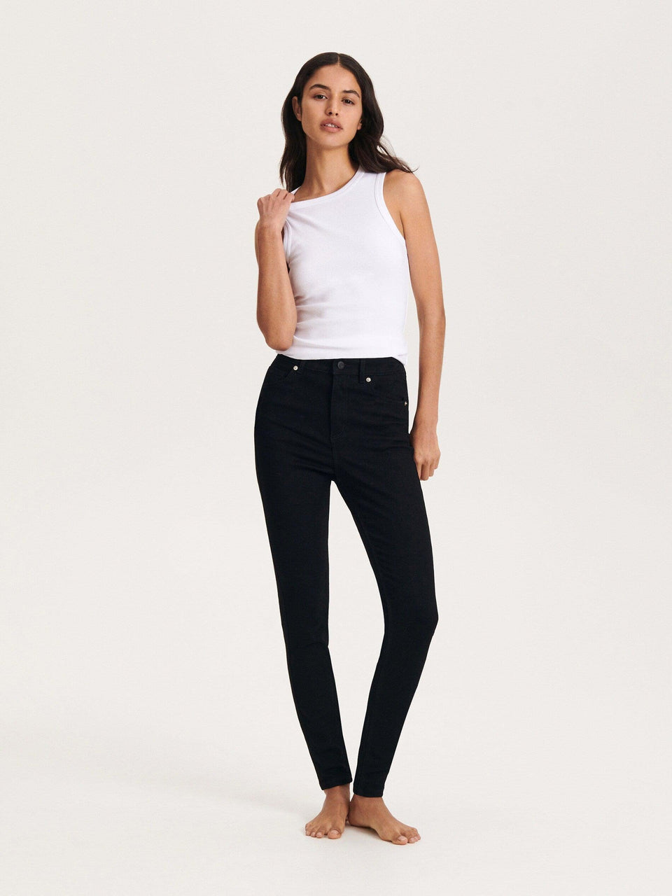 Woman wearing a white tank top and black jeans on a white background