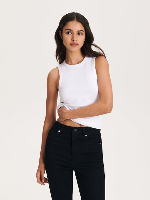 Woman wearing a white sleeveless top and black pants on a plain background