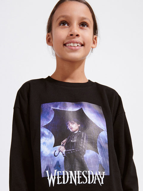 Child wearing a black sweatshirt with a graphic design and the word 'WEDNESDAY' on a light gray background