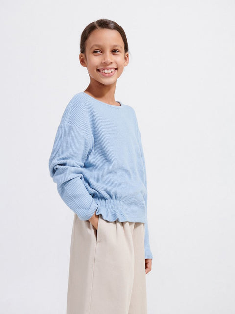 Young girl wearing a light blue sweater and beige pants on a white background