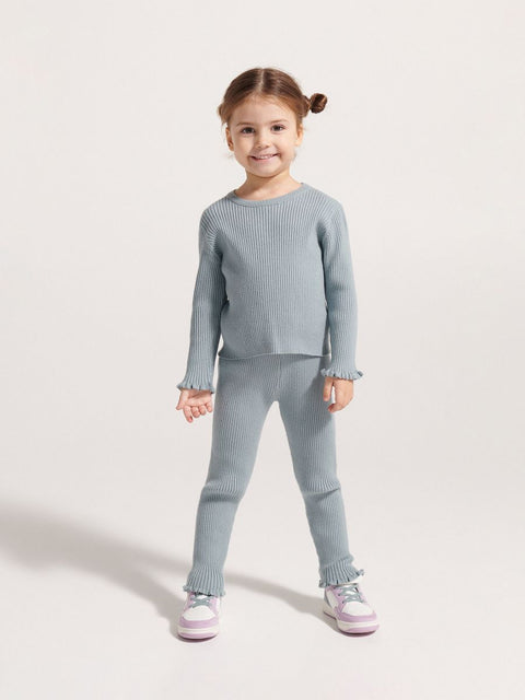 Young girl wearing a gray ribbed sweater and pants on a white background