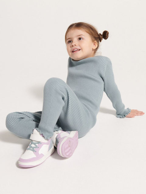 Young girl wearing a light blue ribbed outfit with white sneakers on a white background