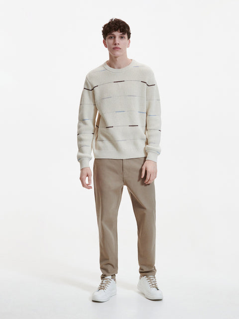 Person wearing a patterned sweater and beige pants on a white background