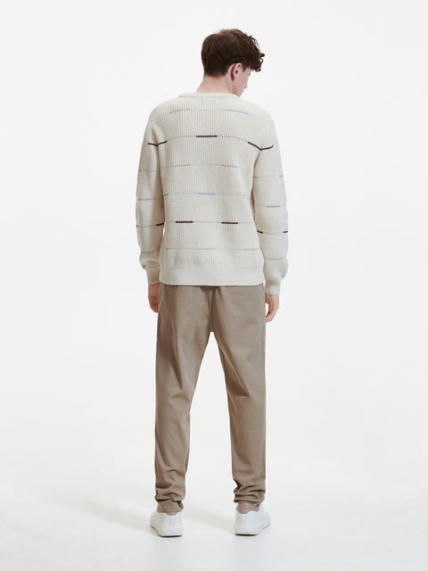 Person wearing a patterned sweater and beige pants on a white background