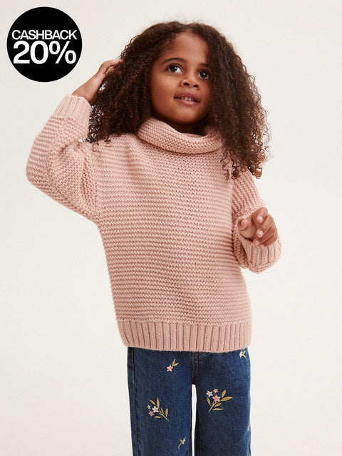 Young girl wearing a pink knitted sweater and blue jeans with floral embroidery on a white background
