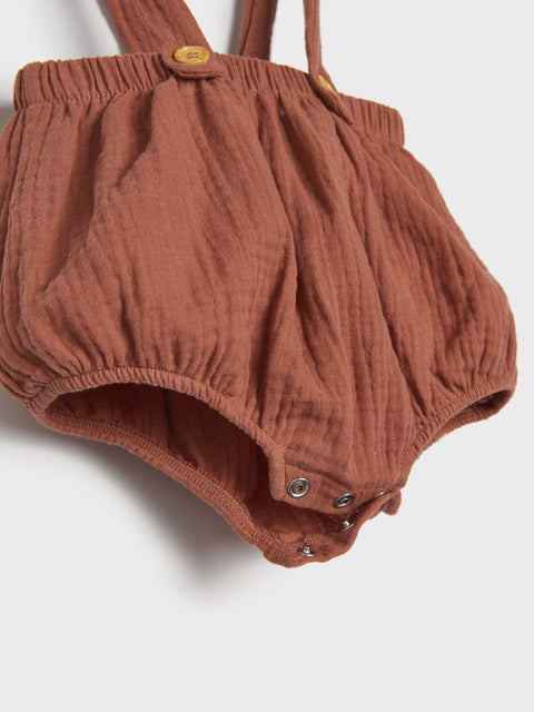 Brown baby romper with suspenders on a light gray background