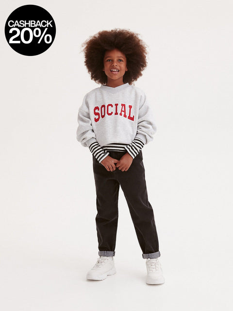 Child wearing a gray sweatshirt with 'SOCIAL' text, black pants, and white sneakers on a white background