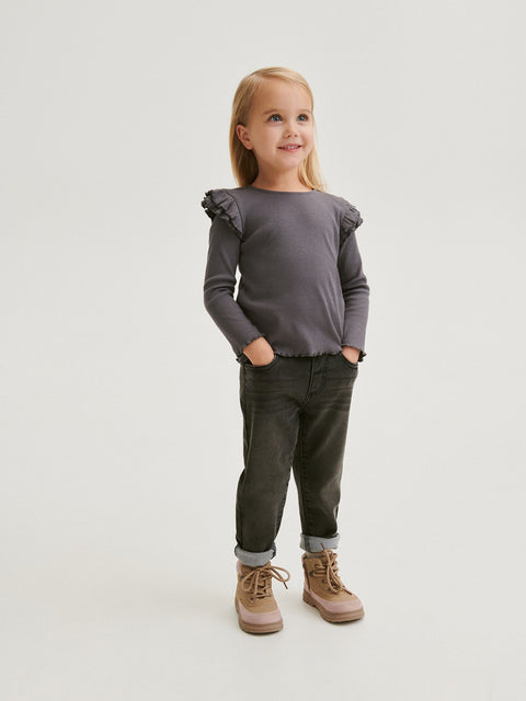 Young girl wearing a gray ruffled shirt and green pants on a white background